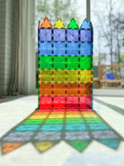 A tall tower built from colorful, translucent Magna-Tiles casting a vibrant rainbow pattern across the floor.