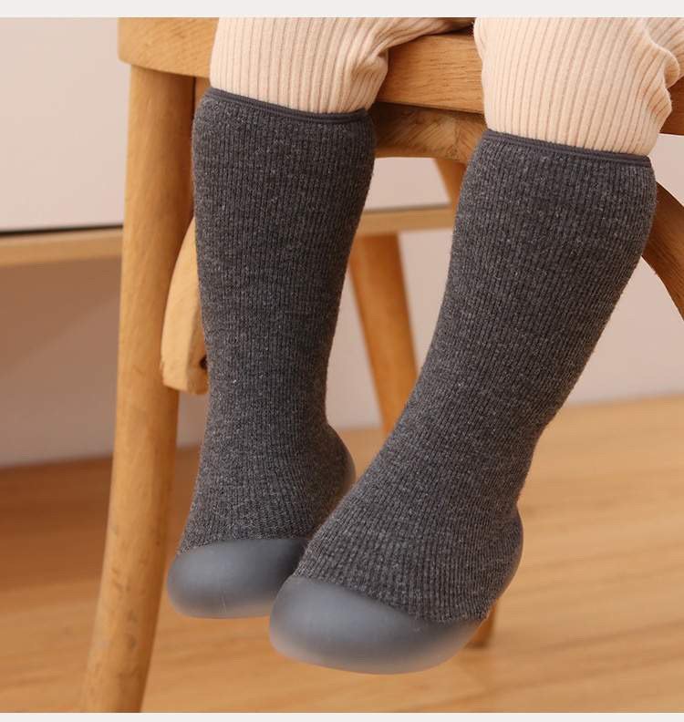 Person wearing dark gray socks with blue toes on a wooden chair.