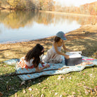 Two children at a picnic by a lake with a cooler box.