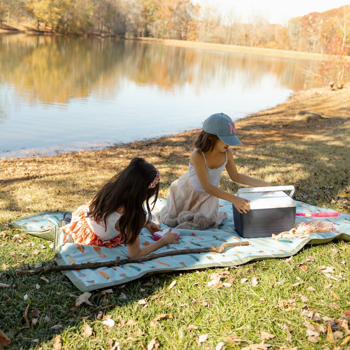 Two children at a picnic by a lake with a cooler box.