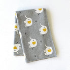 A folded gray fabric cloth featuring a playful pattern of white elephants with yellow trunks and small black bird silhouettes, displayed on a textured white background.