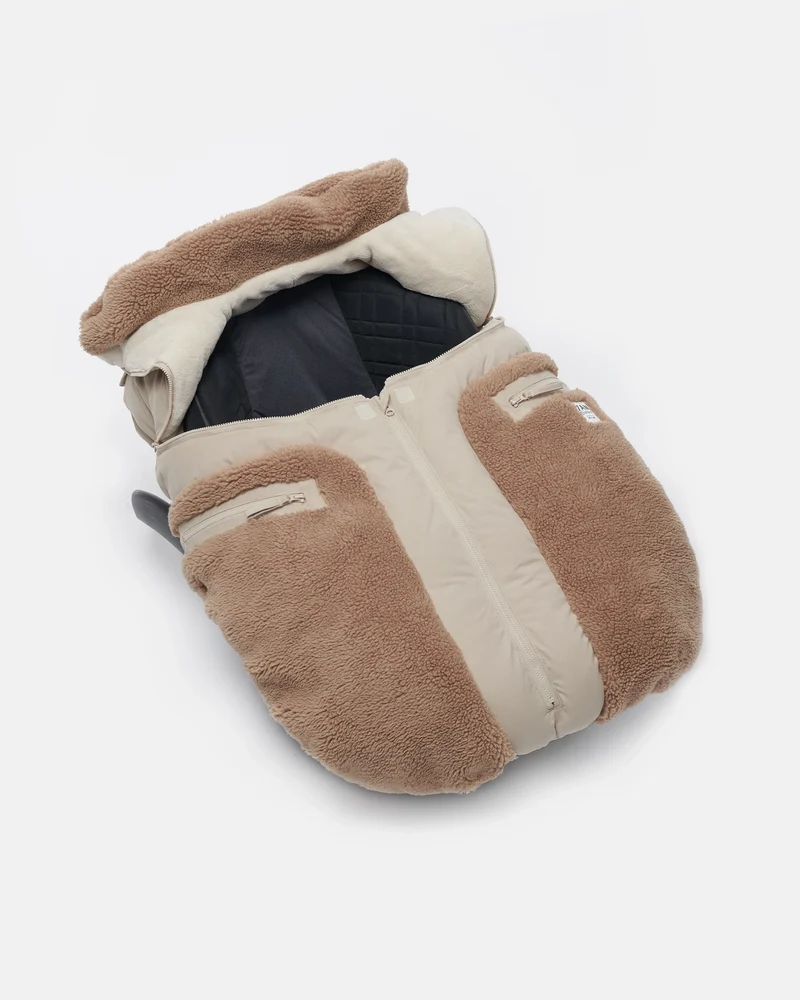 Benji Applique Car Seat Cocoon by 7AM Enfant featuring an oat-colored and brown weatherproof outer shell with plush brown sherpa fleece trim around the collar and a front zipper detail.
