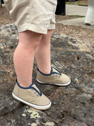 Child wearing beige sneakers with blue accents on a stone surface