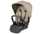 A Peg Perego infant car seat in a light beige/tan fabric with a black handle and black harness straps, shown on a clean white background.