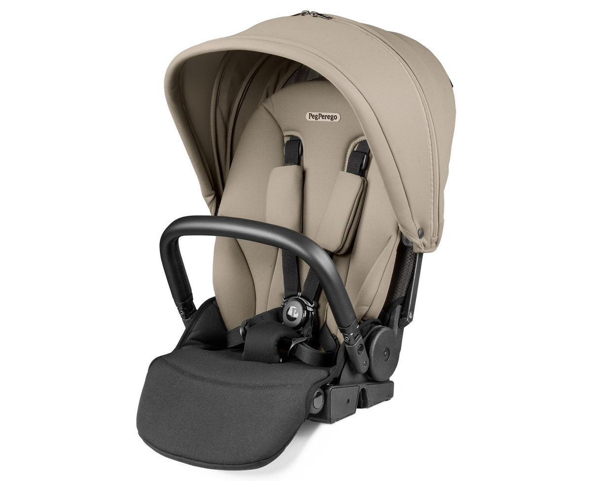 A Peg Perego infant car seat in a light beige/tan fabric with a black handle and black harness straps, shown on a clean white background.