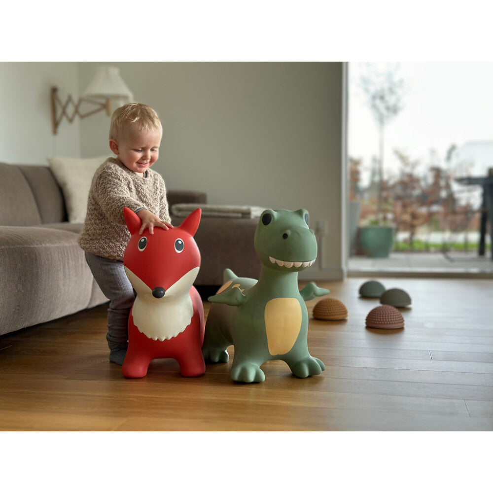 Child playing with a red animal-shaped toy and a green dinosaur toy on a wooden floor.