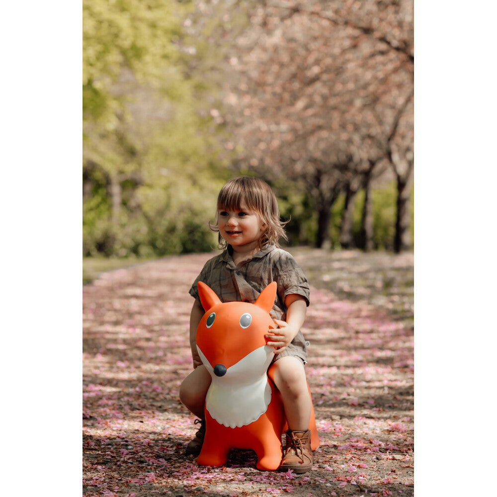 Child holding a fox-shaped toy in a park with cherry blossoms