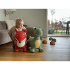 Child playing with a red fox and green dinosaur toy in a living room.
