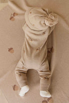 Baby in a beige outfit with matching hat and shoes on a beige background
