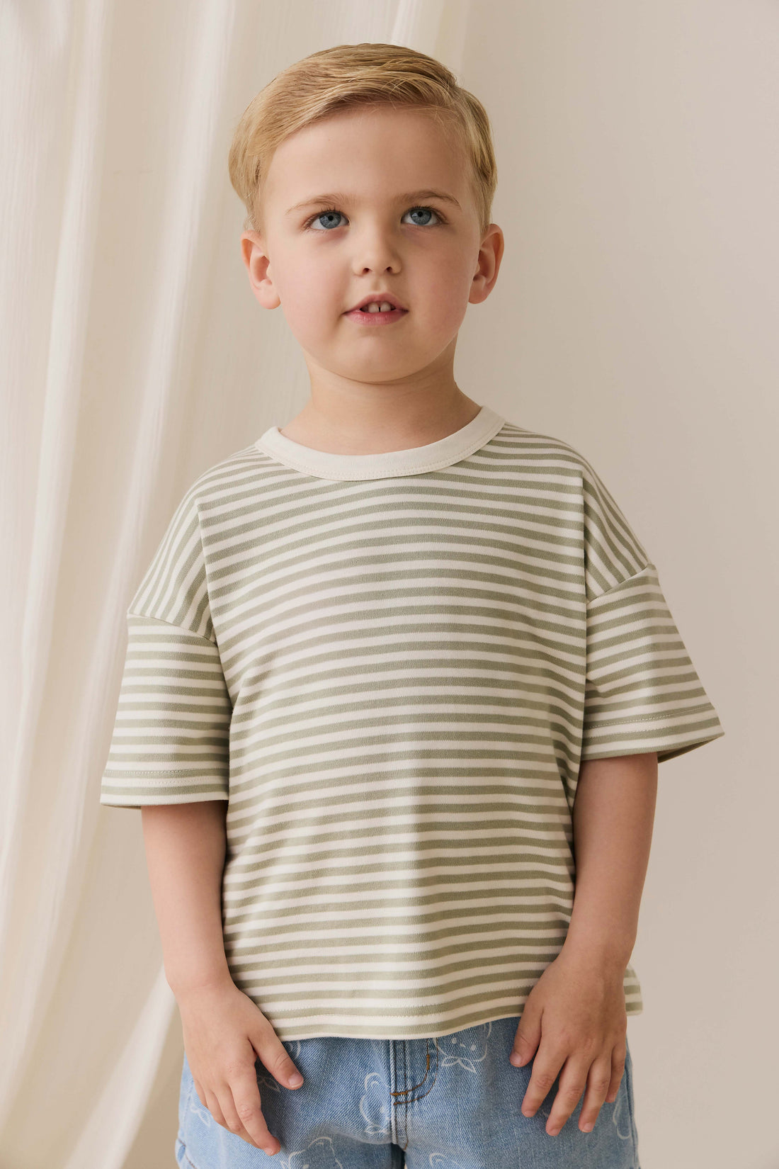Young boy wearing a striped shirt and jeans against a plain background