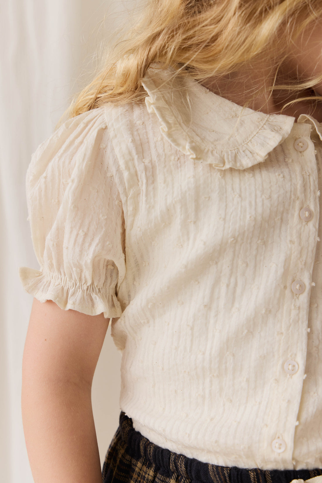 Close-up of a person wearing a cream-colored blouse with ruffled collar and puff sleeves.