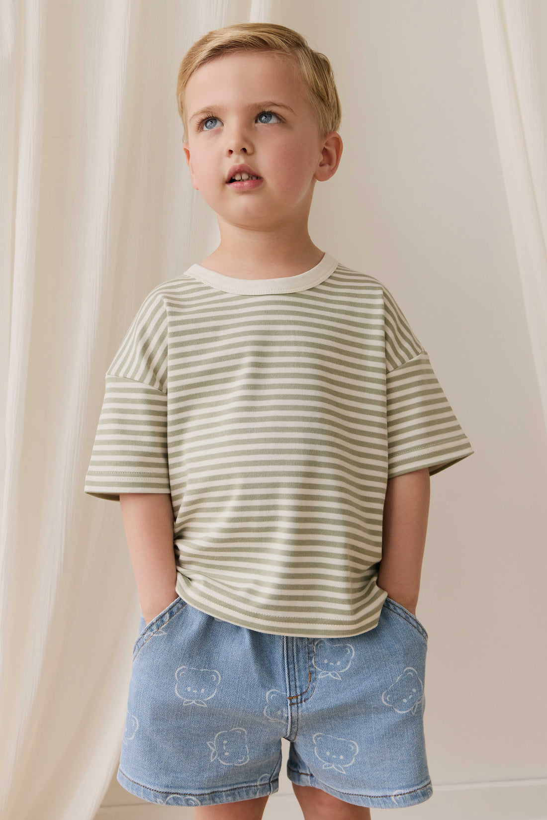 Child wearing a striped shirt and denim shorts against a neutral background