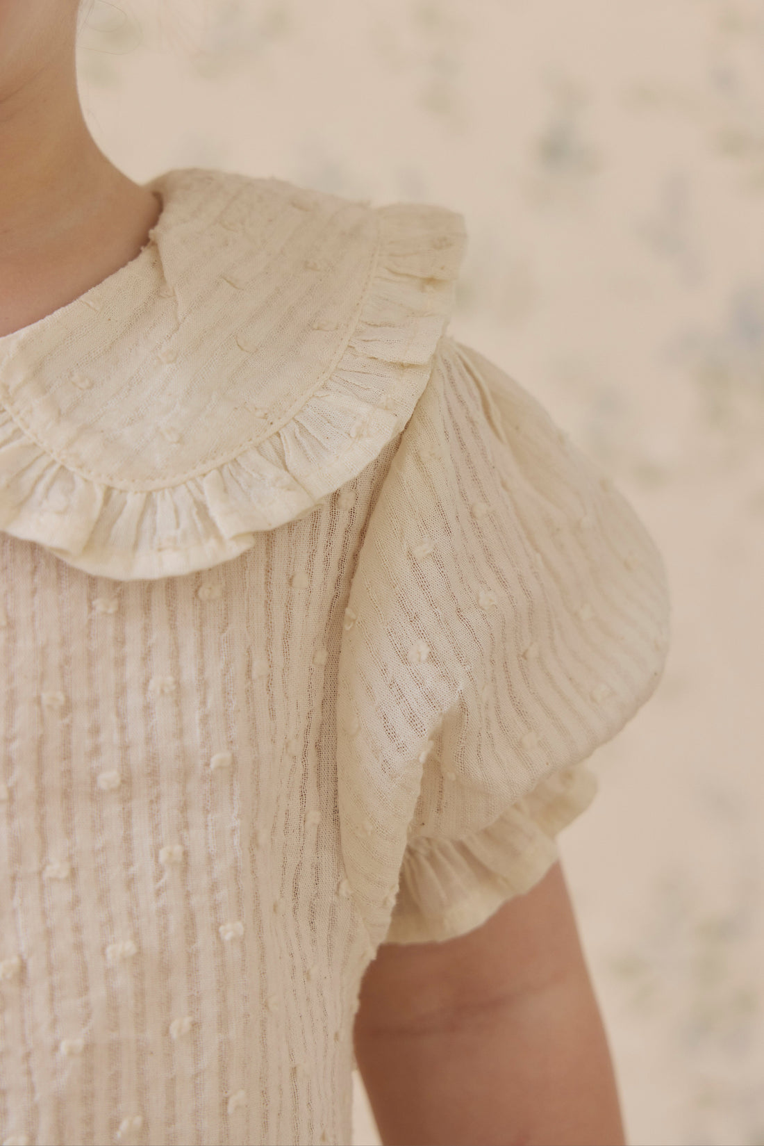 Close-up of a textured beige blouse with a ruffled collar.