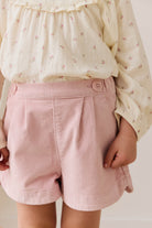 Person wearing a light-colored blouse with floral patterns and pink shorts on a plain background