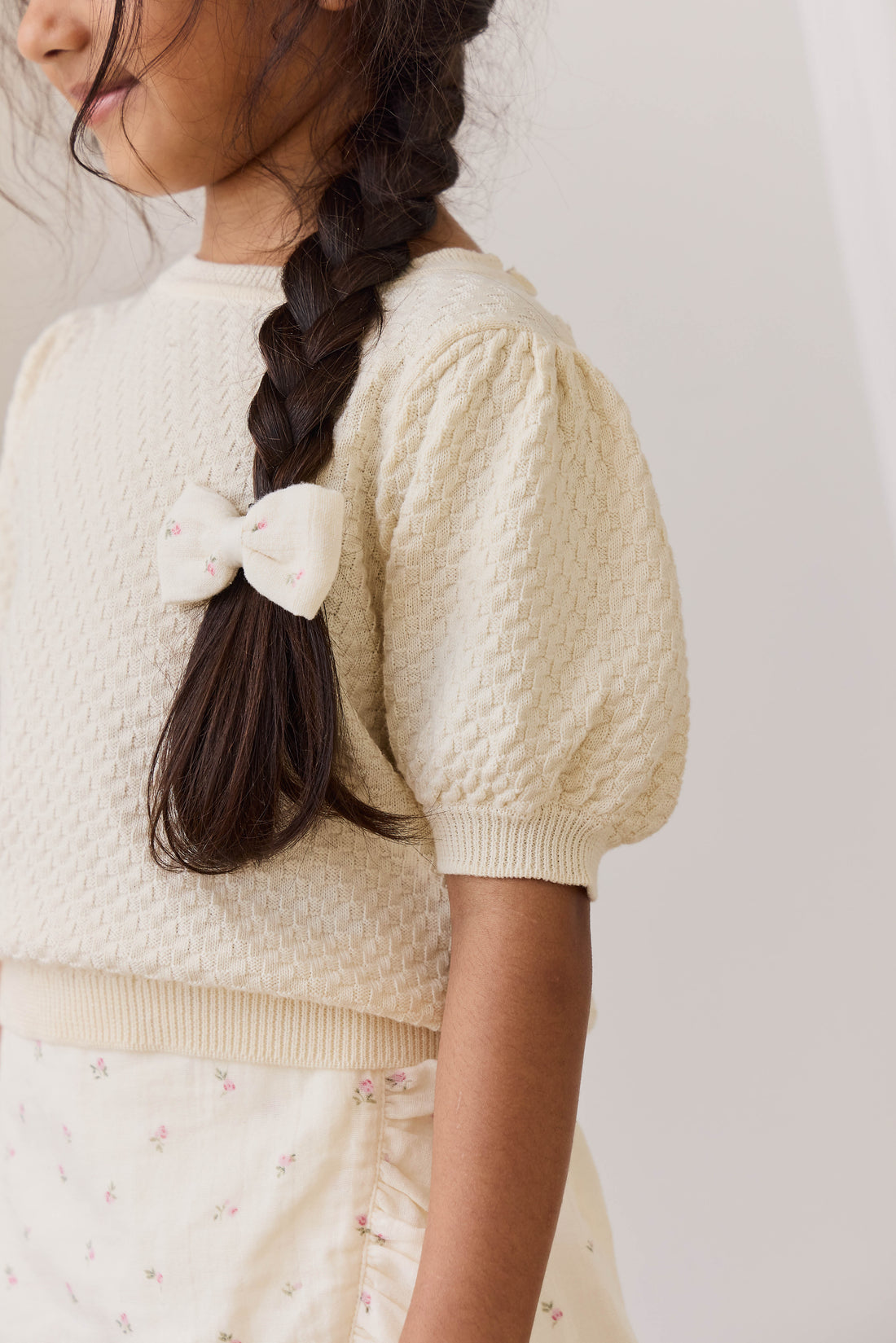 Person wearing a cream-colored knitted cardigan with a plain background