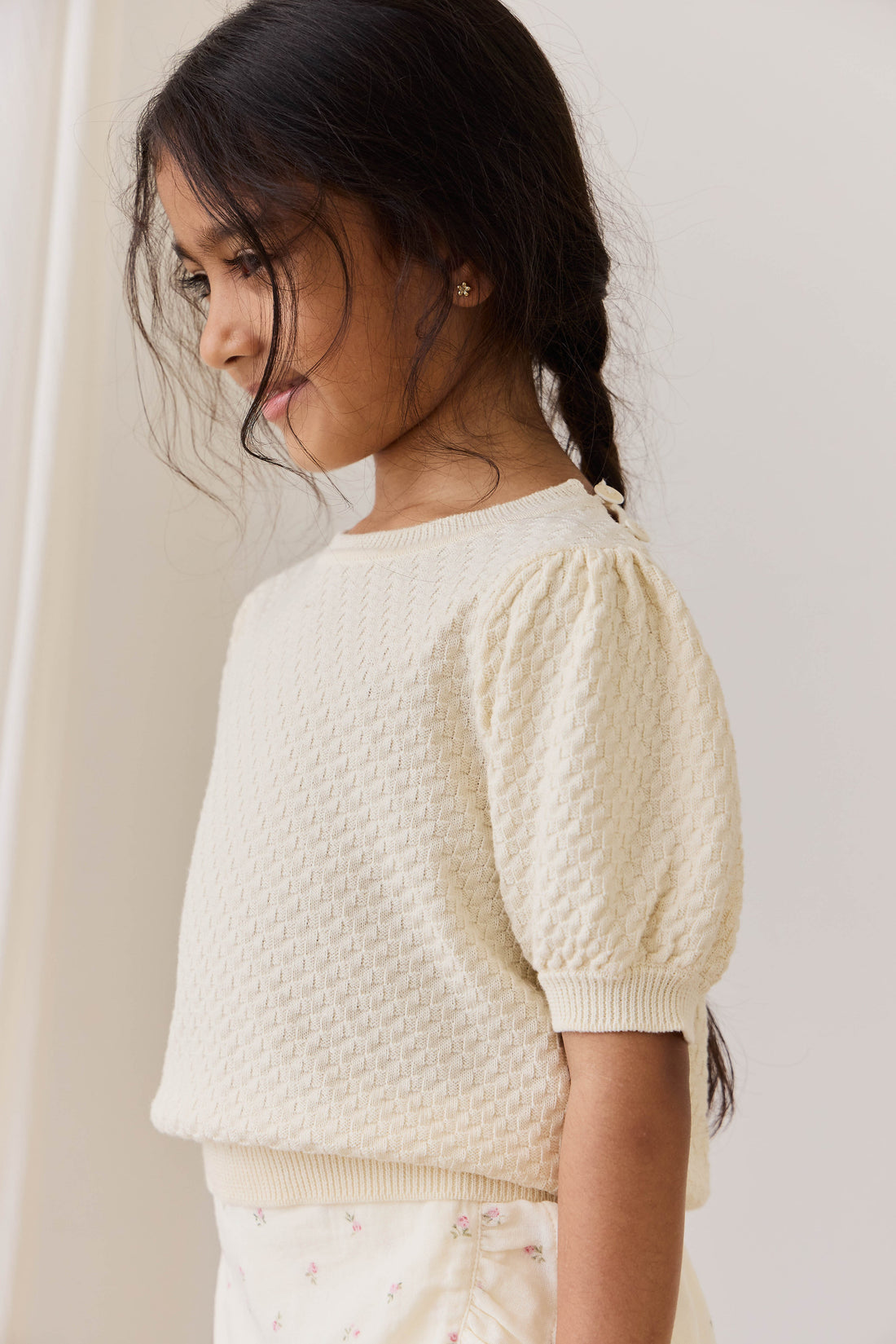 Young girl wearing a textured white top against a plain background