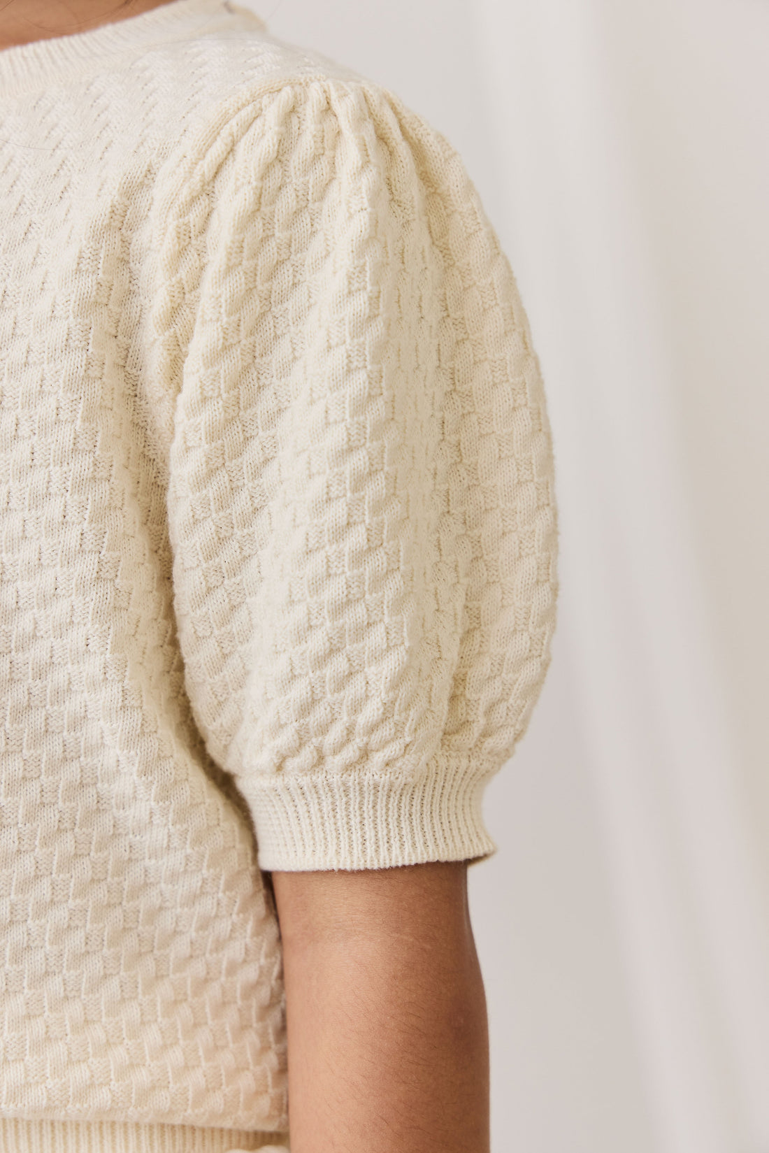 Close-up of a cream-colored textured sweater with puff sleeves on a plain background