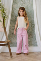 Young girl wearing a white top and pink pants with a floral pattern in a room with a decorative wall.