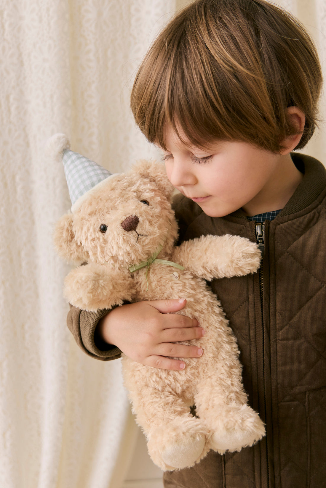 Child holding a teddy bear with a neutral background