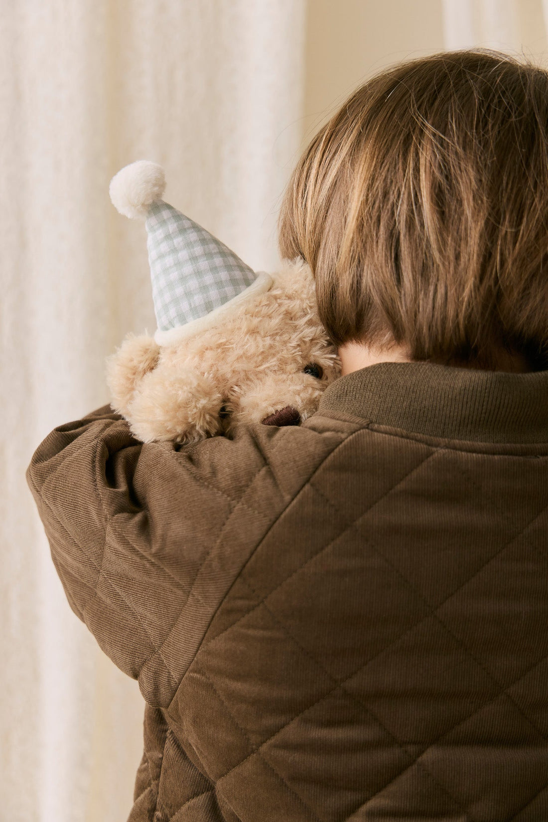 Person holding a teddy bear with a small hat indoors