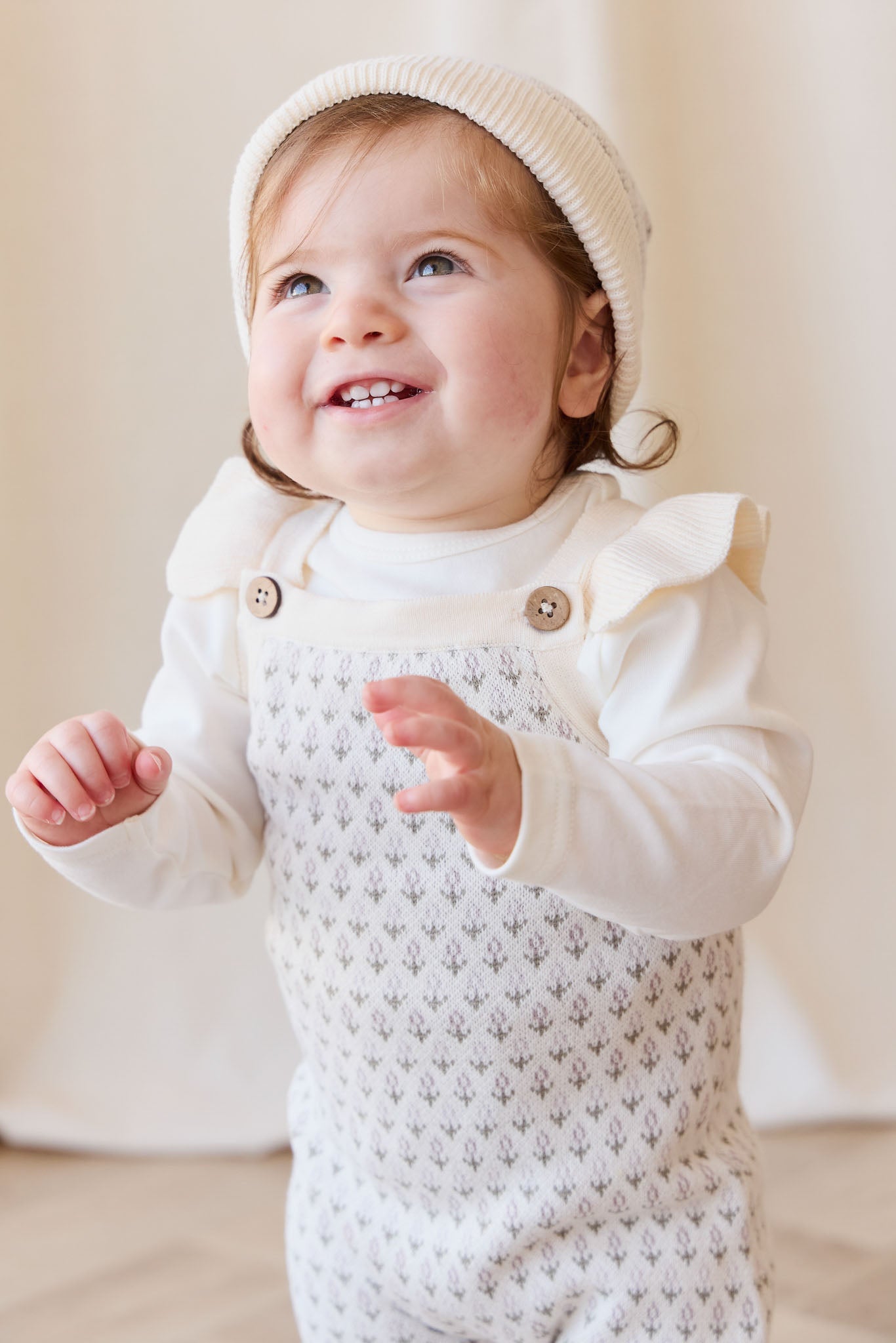 Baby wearing a white knit outfit with a textured pattern on a neutral background