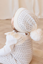Newborn baby wrapped in a white blanket with a matching hat on a light wooden floor.