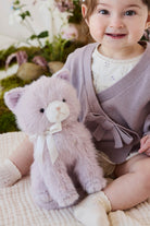 A toddler wearing a knit violet cardigan and white bunny-ear headband cuddling a soft violet-toned plush kitty toy by Jamie Kay.
