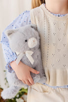 A child wearing a cream-colored knit vest and a blue patterned blouse while holding the soft grey plush kitten toy.