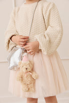 Child wearing a textured cream sweater and pale pink tulle skirt, holding the Snuggle Bunnies Arthur Keyring by Jamie Kay attached to a metallic silver star-shaped handbag.