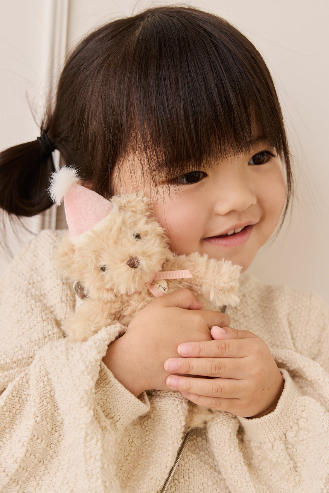Child wearing a textured cream sweater and holding the Snuggle Bunnies Arthur Keyring by Jamie Kay close to her chest.