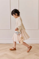 Child walking in profile view, wearing a textured cream sweater, a pale pink tulle skirt, and brown shoes, carrying a metallic silver star-shaped handbag with the Snuggle Bunnies Arthur Keyring by Jamie Kay clipped to it.