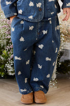 Child wearing blue jeans with white patterns and brown shoes, standing in a garden.