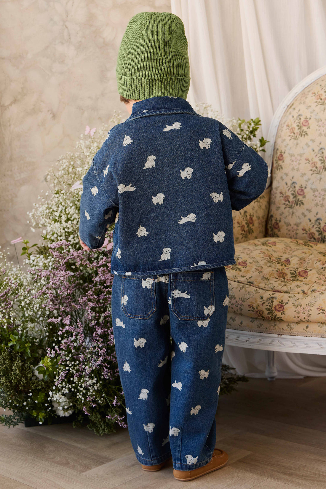 Child wearing a blue outfit with animal patterns in a room with flowers and a sofa.