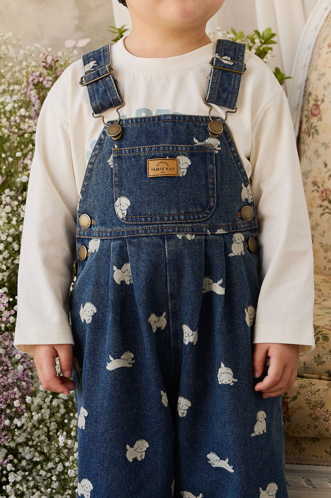 Child wearing blue denim overalls with white patterns, standing in a garden.