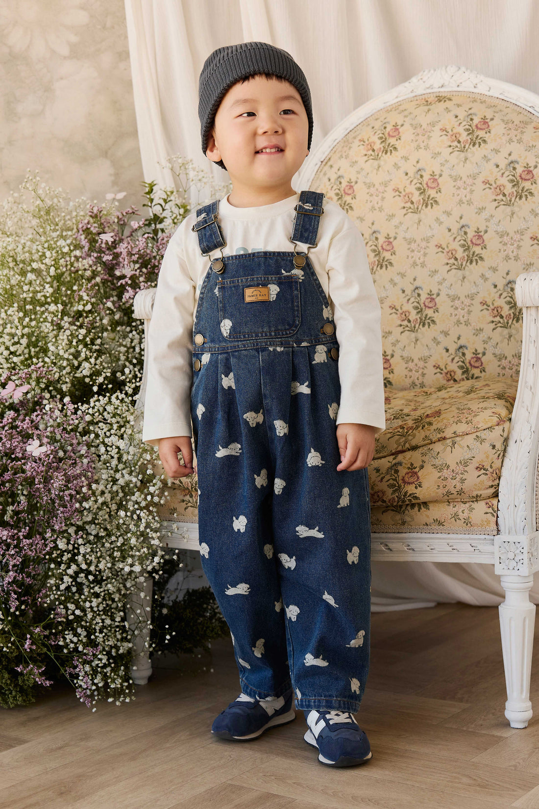 Child wearing a blue denim outfit with animal prints in a room with floral wallpaper and flowers.