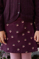 Person wearing a dark purple skirt with cherry pattern and matching cardigan.
