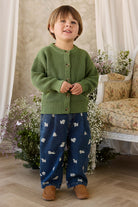 Child wearing a green knitted cardigan and blue pants with animal patterns, standing in a decorated room.