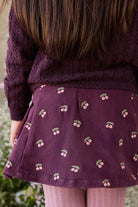 Person wearing a dark purple sweater and skirt with cherry pattern