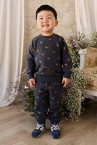 Child wearing a navy sweater and pants with small patterns, standing in a decorated room with flowers and a chair.