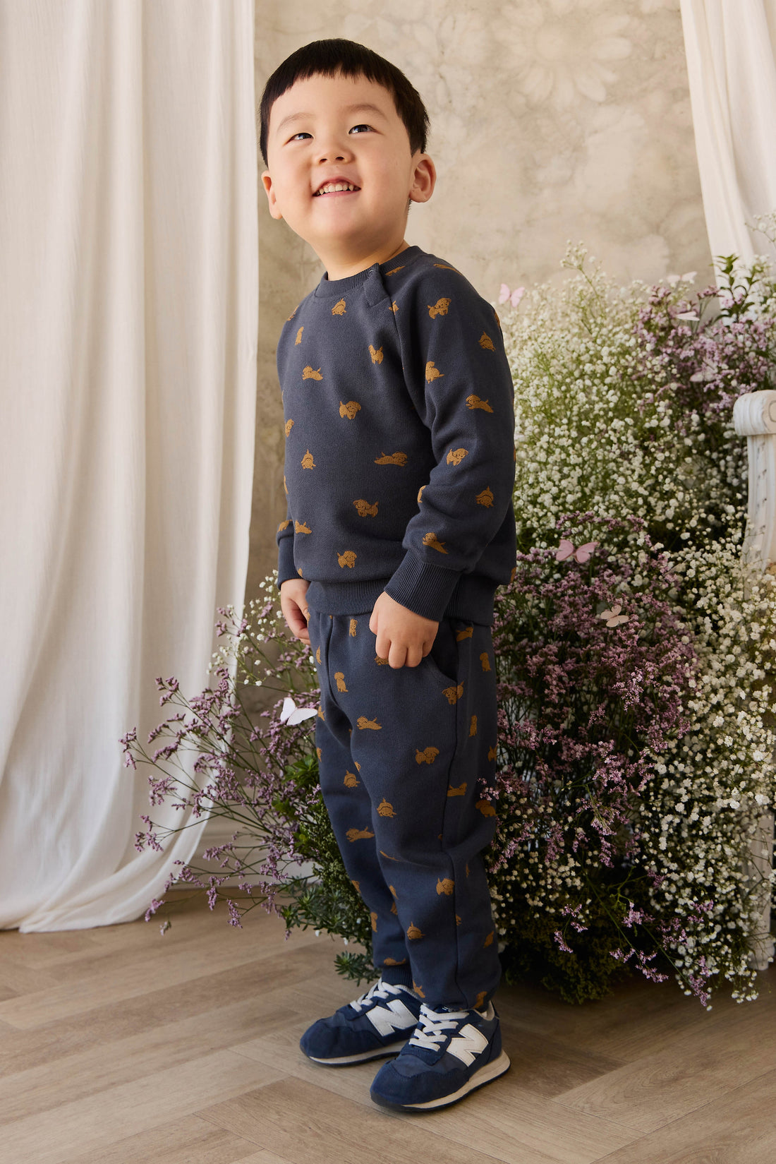 Child wearing a navy blue sweater and pants with orange patterns, standing in front of flowers.