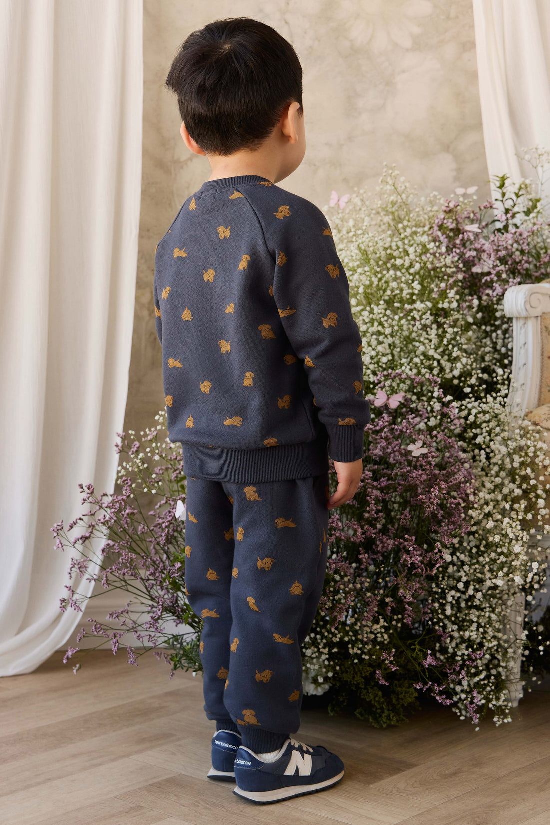 Child wearing a navy blue outfit with gold patterns standing in front of floral arrangements.