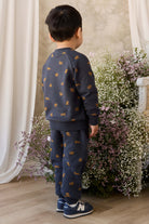 Child wearing a navy blue outfit with gold patterns standing in front of floral arrangements.