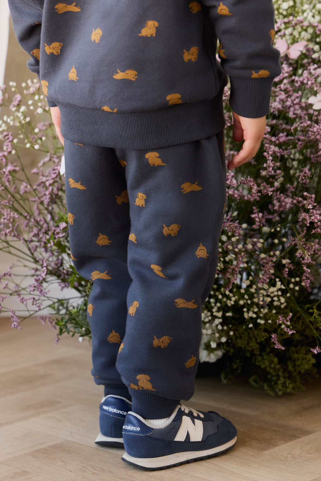 Child wearing navy blue outfit with orange dog pattern, standing in front of floral background