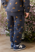 Child wearing navy blue outfit with orange dog pattern, standing in front of floral background