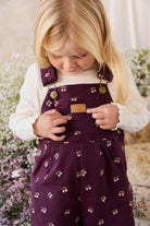 Young girl wearing a purple dress with cherry pattern, standing in a garden.
