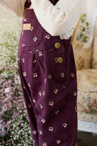 Purple overalls with cherry pattern worn by a person, blurred background