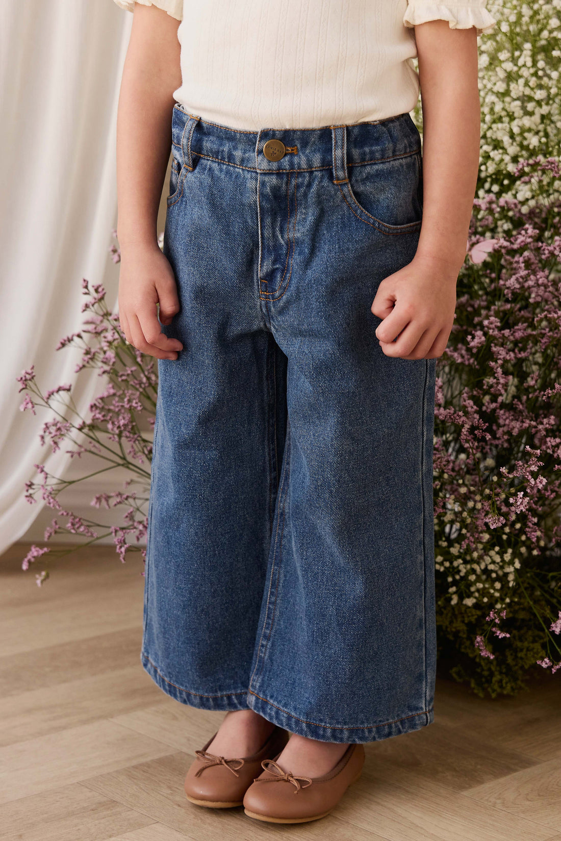 Person wearing blue jeans and a white top in front of floral decorations.