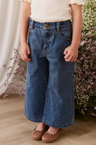 Person wearing blue jeans and a white top in front of floral decorations.