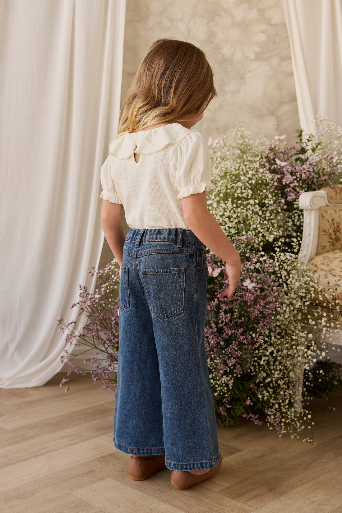 Woman in a white blouse and blue jeans standing in a room with floral decorations.