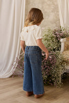 Woman in a white blouse and blue jeans standing in a room with floral decorations.